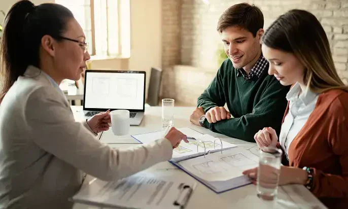 A business meeting in a bright room, focusing on documents and plans, with a laptop, glasses of water, and discussions underway.