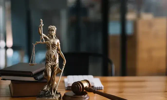 A bronze statuette of Lady Justice holding scales and a sword, accompanied by a wooden gavel on a desk with books and notepads.